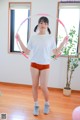 A woman in a white shirt and orange shorts holding a hula hoop.