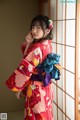 A woman in a red kimono standing in front of a window.